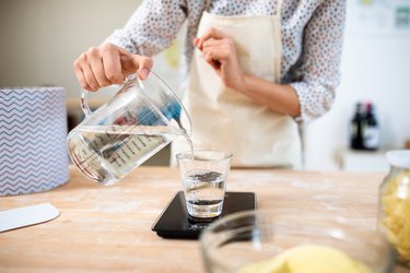 Close view of a chef measuring the weight of a glass of water in the kitchen