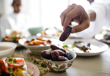 hand reaching for dates in a bowl with food spread for a Muslim diet