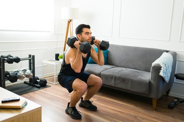 fit person wearing all black doing a dumbbell squat thruster in a living room