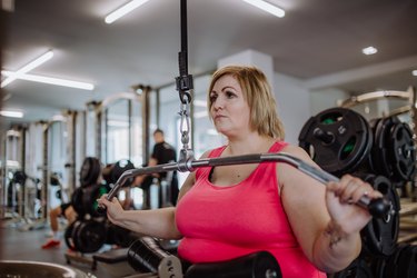 Adult athlete performing lat pulldown in pink tank top at the gym.