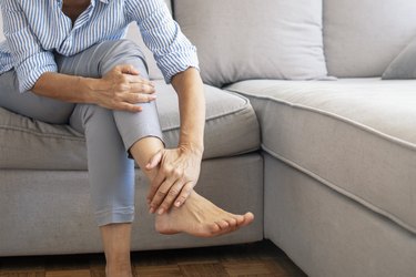 close view of a person sitting on a couch and rubbing their foot because they have pins and needles in their foot