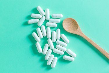 Probiotic tablets and capsules and wooden spoon on bright light green background.