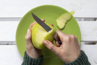 Close-up of female hands peeling a green apple.