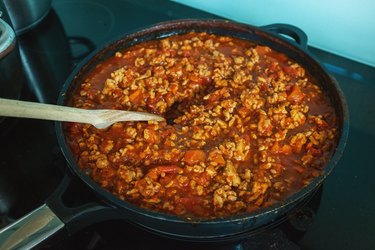 an overhead photo of bolognese sauce in a large skillet on a stove with a wooden spoon
