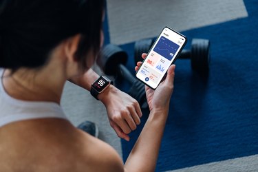 Over the shoulder view of young woman using exercise an tracking app to track her strength sessions, wondering how long should a weightlifting workout last to be effective