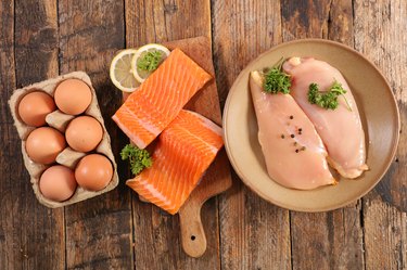 selection of animal proteins, salmon, chicken and eggs, on wood