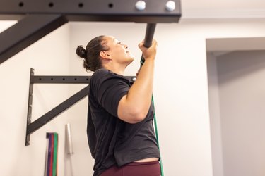 Person doing pull-ups with resistance band at gym as example of compound back exercises..