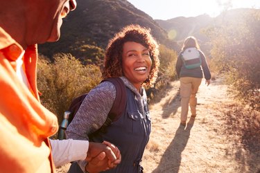 Woman Helping Man On Trail As Group Of Senior Friends Go Hiking In Countryside Together, as an example of a healthy aging community