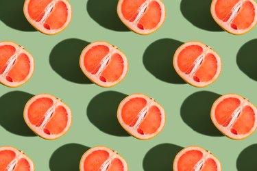 A pattern of half a grapefruit on a green background with a hard shadow.