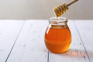 Jar of honey with a honey dipper on a wooden table as a natural fat lip remedy