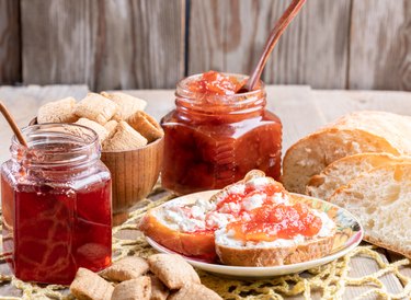 Toasts and jar with strawberry and apple jams, square snacks on yellow knitted napkin on rustic wooden table.