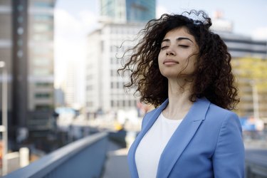 a person wearing a blue blazer and white shirt with their eyes closed takes a deep belly breath outside to de-stress