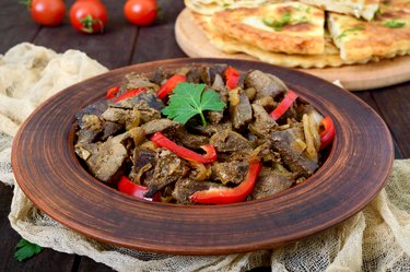 Pieces of fried vitamin A-rich liver with onions and fresh bell peppers on a plate.