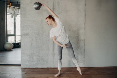 Red haired beautiful woman with fitball performing barre exercises