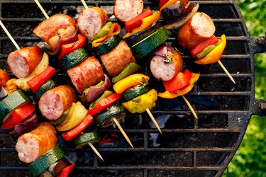 Grilled skewers of meat, sausages and various vegetables on a grill plate, outdoors, top view.