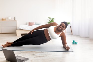 plus-size black woman doing a side plank in front of laptop at home