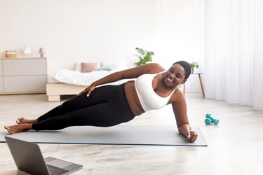 woman doing a side plank exercise in front of laptop at home