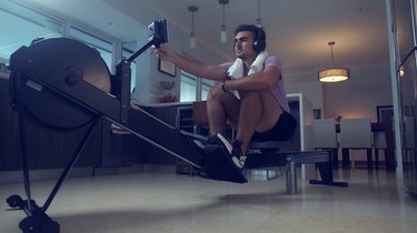 man adjusting settings on a rowing machine at home