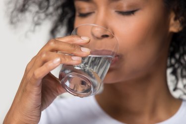 a close up of a person wearing a white t-shirt drinking a glass of water