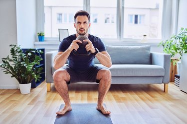 fit man doing a kettlebell goblet squat and working out at home