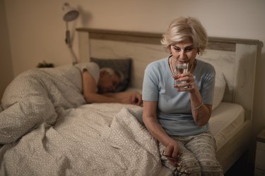 Older woman drinking a glass of water in bed because she has hiccups while sleeping
