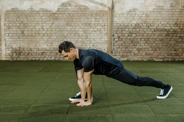 buff person with short hair wearing pants and a t-shirt does a lunge full-body stretch