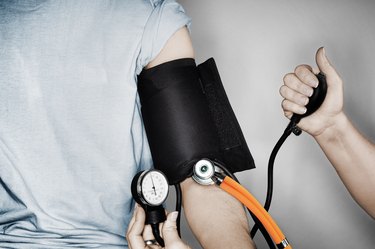 a close up photo of a person wearing a gray t-shirt having their blood pressure checked with a black cuff with an orange tube