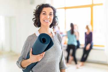 A smiling, mature woman holding a yoga mat, to represent exercise during menopause