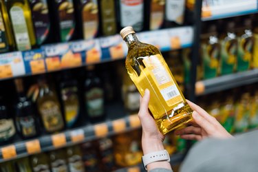 Close up of hands holding a cooking oil bottle, deciding between canola oil vs. peanut oil, reading the back of the label.