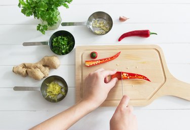 person cutting hot peppers on wooden board with salsa ingredients