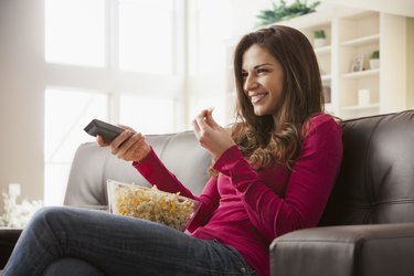 Woman watching television on sofa eating popcorn
