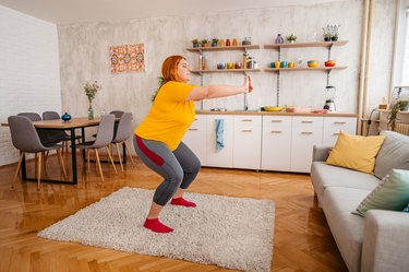 Exerciser doing squat in living room on fuzzy rug.
