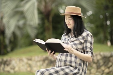 A pregnant woman sits in a park and reads her journal