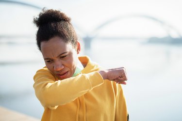 Middle-aged runner in a yellow sweatshirt coughing up phlegm into their elbow while running.