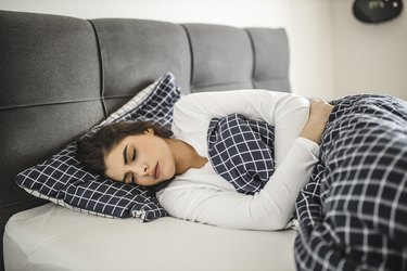 Young woman lying down on her bed and suffering from period pains at home