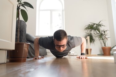 a front view of an adult wearing a gray t-shirt and black glasses doing wide push-ups at home