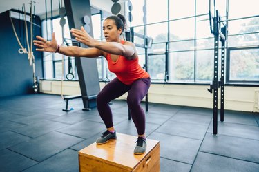 Person wearing a red tank top and purple leggings doing a box jump as one of the best plyometric exercises for runners.