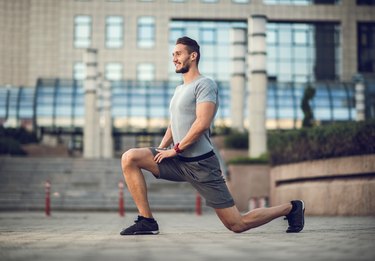 Happy male athlete exercising lunges on the city street.