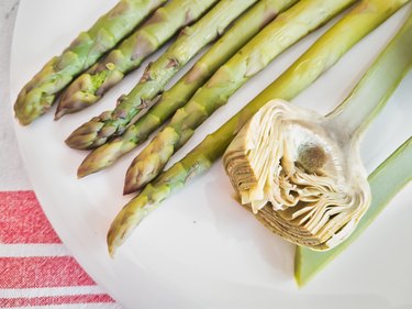 Asparagus and artichokes on a white plate on top of a tablecloth with red strips