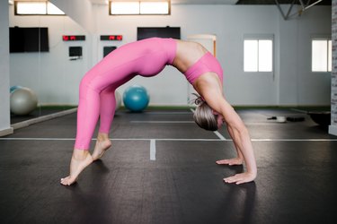 flexible person in pink sports bra and leggings doing wheel pose in yoga, a bad yoga pose for osteoporosis