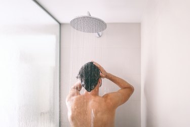 Man taking a shower washing hair with shampoo product under water falling from luxury rain shower head