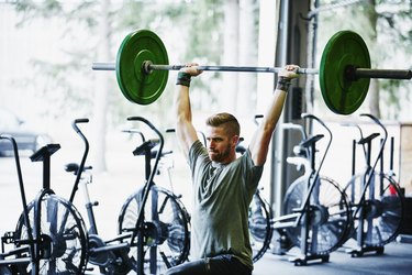 Man doing lunges with barbell overhead in gym