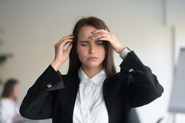 Stressed millennial female office worker suffering from sudden head pain.