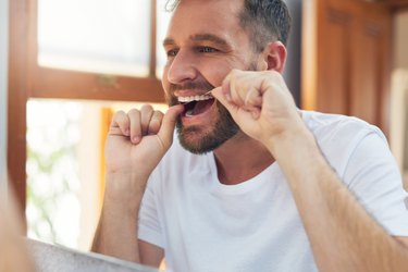 man in the bathroom flossing before brushing his teeth