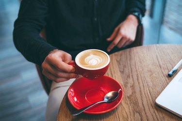 Person holding coffee in red mug at wooden cafe table with ADD and caffeine wondering add and caffeine what is alza 54 used for