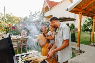 A family of three cooking food on the grill in their backyard