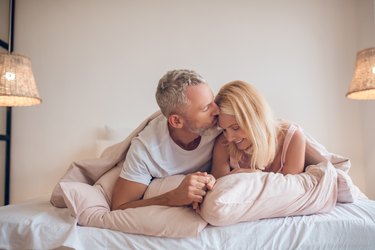 Grey-haired man and a blonde woman lying on the bed and looking romantic