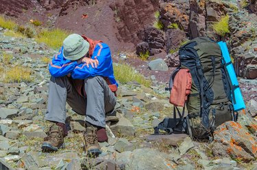 a trekker sits on a rock next to a backpack resting after feeling the effects of high altitude on the body
