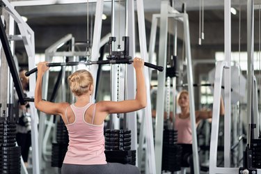 Athlete performing lat pulldown in gym wearing a pink tanktop.