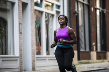 Person wearing purple sports bra and black leggings running outside.